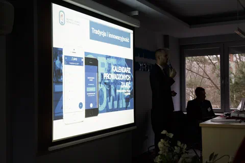 Prezentacja multimedialna wyświetlana na ekranie projekcyjnym w przyciemnionej sali.