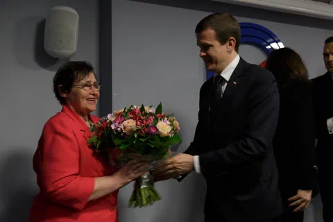 Wręczenie bukietu kwiatów uczestniczce uroczystości na tle znaku Instytutu Sportu.
