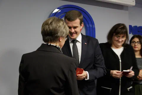 Wręczenie odznaczenia kolejnej wyróżnionej osobie w obecności przedstawicielek organizatora.