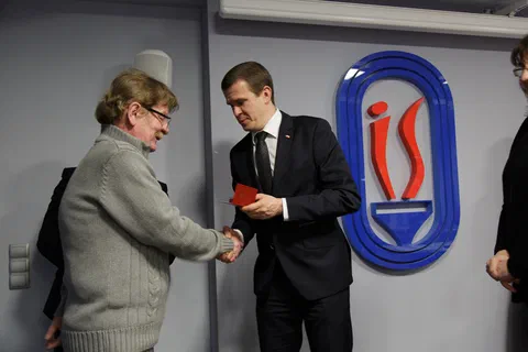 Uścisk dłoni i wręczenie odznaczenia pracownikowi w szarym swetrze.