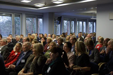 Widok na wypełnioną salę konferencyjną z uczestnikami uroczystości jubileuszowej.