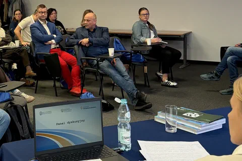 Troje uczestników rozmawiających w kręgu za stołem z laptopem i materiałami szkoleniowymi.