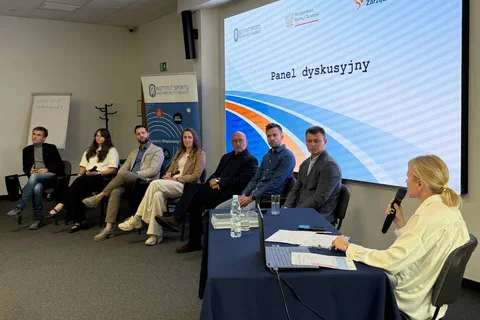 Sześcioro panelistów siedzących w rzędzie przed ekranem z napisem „Panel dyskusyjny” oraz moderatorka przy stoliku.