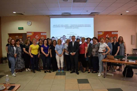 Grupowe zdjęcie uczestników i prowadzących szkolenie Akademii Zarządzania Sportem w sali wykładowej przed ekranem z prezentacją o przepisach podatkowych (VAT, CIT, PIT i ZUS w 2022 r.) w działalności sportowej