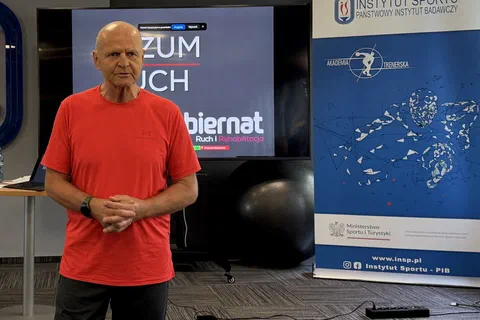 Wykładowca prowadzący prelekcję na tle ekranu i ścianki z logotypami Instytutu Sportu – PIB oraz Akademii Trenerskiej.