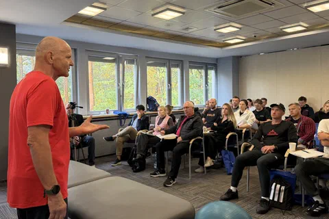 Wykładowca omawiający zagadnienia praktyczne przed grupą uczestników siedzących w półkolu.