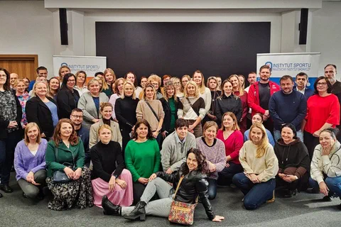 Wspólne zdjęcie dużej grupy uczestników szkolenia ustawionych w kilku rzędach w sali konferencyjnej.