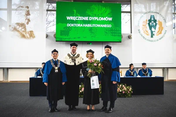 Uroczystość wręczenia dyplomów doktora habilitowanego w AWF Warszawa: dr hab. Dorota Sadowska w todze z bukietem kwiatów i dyplomem w otoczeniu władz uczelni.