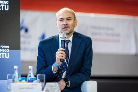 Zbliżenie na uczestnika debaty wypowiadającego się do mikrofonu przy stoliku z wodą.