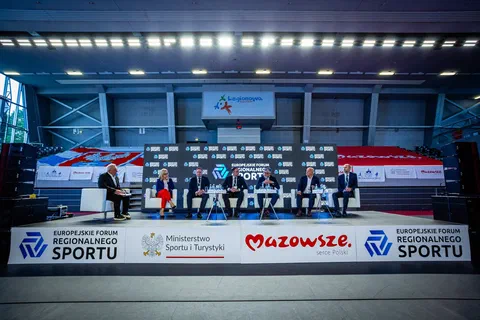 Szeroki kadr sceny z sześciorgiem uczestników debaty siedzących w fotelach na tle ekranu Europejskiego Forum Regionalnego Sportu.