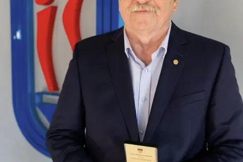 Wyróżniony w marynarce prezentujący złoty medal w otwartym etui na tle znaku Instytutu Sportu.