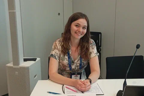 Uczestniczka siedząca za stołem prezydialnym z mikrofonem i tabliczką imienną przed sesją naukową.
