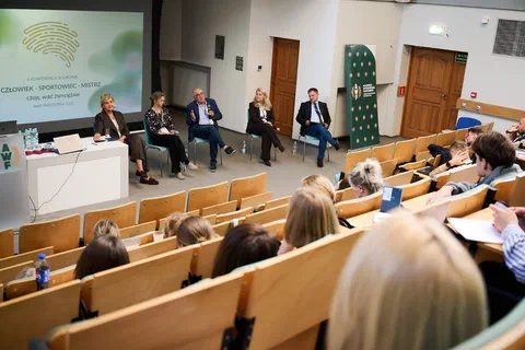 Pięcioro uczestników panelu dyskusyjnego siedzących na krzesłach przed widownią w auli wykładowej.