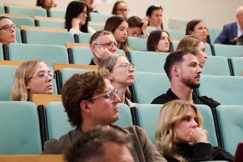 Słuchacze siedzący w rzędach amfiteatralnej auli wykładowej podczas konferencji.