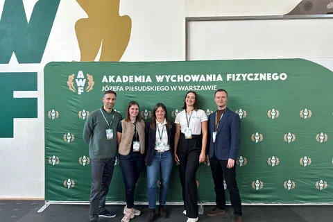 Pięcioro prelegentów pozujących wspólnie na tle zielonej ścianki Akademii Wychowania Fizycznego w Warszawie.