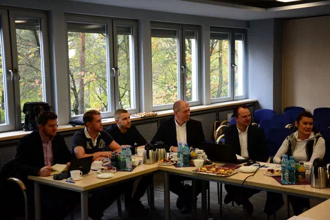 Uczestnicy posiedzenia siedzący przy stole konferencyjnym z laptopami pod oknami sali.
