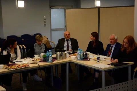 Część stołu konferencyjnego z uczestnikami przeglądającymi materiały robocze.