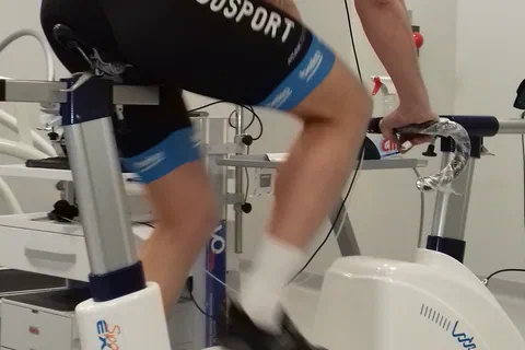 Zawodnik w stroju kolarskim i masce spirometrycznej podczas testu na cykloergometrze.