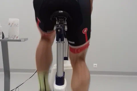 Zawodnik w czerwonej koszulce kolarskiej pedałujący na cykloergometrze podczas testu laboratoryjnego.