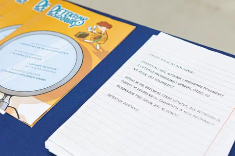 Zbliżenie na teczkę i kartę zadań edukacyjnych „Detektyw Zdrówko” leżące na stole.