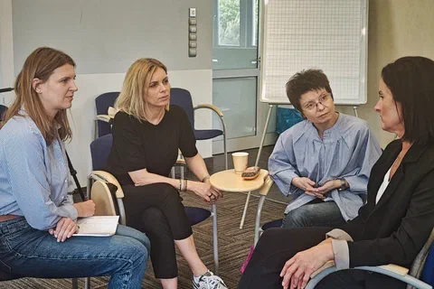 Cztery kobiety dyskutujące w podgrupie obok białej tablicy flipchart.