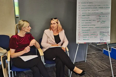 Dwie uczestniczki rozmawiające obok flipchartu zapisanego wnioskami z dyskusji o przywództwie.