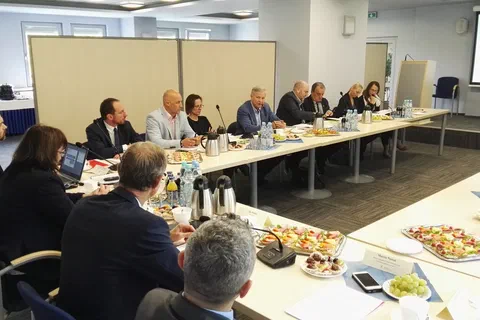 Widok na salę konferencyjną z uczestnikami obradującymi przy stołach ustawionych w podkowę.