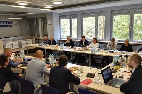 Szeroki kadr sali obrad ze znakiem Instytutu Sportu i ekranem projekcyjnym w tle.