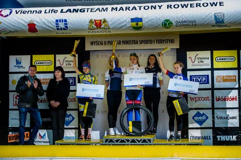 Młode kolarki na podium wyścigu o Puchar Ministra Sportu i Turystyki z pucharami i nagrodami.