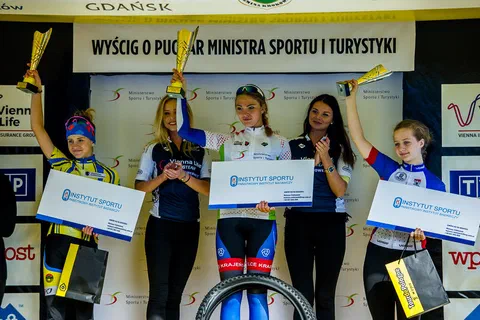 Zbliżenie na trzy zawodniczki na podium prezentujące puchary i bony Instytutu Sportu – PIB.
