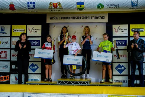 Dekoracja trzech młodych kolarzy na podium w obecności organizatorów i wręczających nagrody.