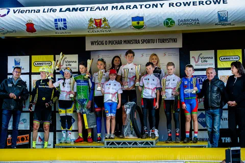 Wspólne zdjęcie nagrodzonych młodych kolarek i kolarzy z organizatorami na podium zawodów.