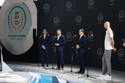 Czterej prelegenci stojący przy mikrofonach na scenie z logo II Europejskiego Kongresu Sportu i Turystyki 2023.