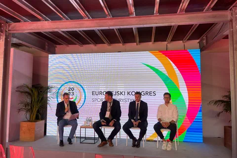 Czterej uczestnicy debaty siedzący na scenie przed ekranem z logo Europejskiego Kongresu Sportu i Turystyki.
