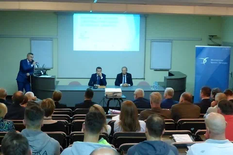 Otwarcie konferencji przy stole prezydialnym przed uczestnikami zgromadzonymi w sali wykładowej.