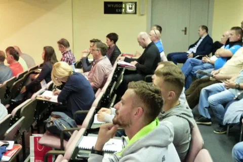 Uczestnicy konferencji siedzący w rzędach sali wykładowej z notatnikami.