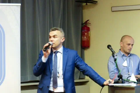 Wystąpienie prelegenta z mikrofonem obok stołu prezydialnego i baneru Instytutu Sportu.