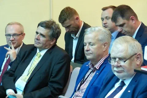 Zbliżenie na uczestników w garniturach przysłuchujących się obradom.