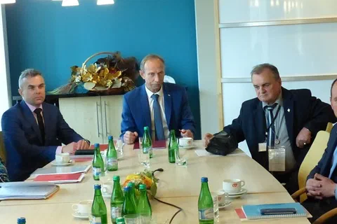Trzej mężczyźni w garniturach prowadzący obrady u szczytu stołu konferencyjnego.