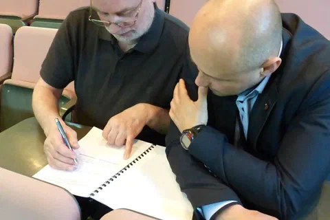 Dwaj uczestnicy na widowni konsultujący notatki w zeszycie szkoleniowym.