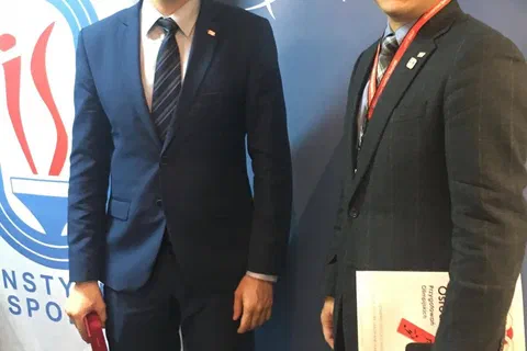 Dwaj uczestnicy w garniturach pozujący na tle roll-upów Instytutu Sportu i Ministerstwa Sportu i Turystyki.