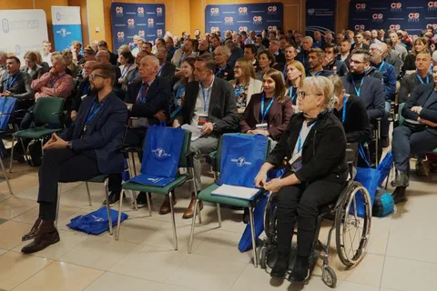 Widok na salę konferencyjną z uczestnikami siedzącymi w rzędach podczas obrad.