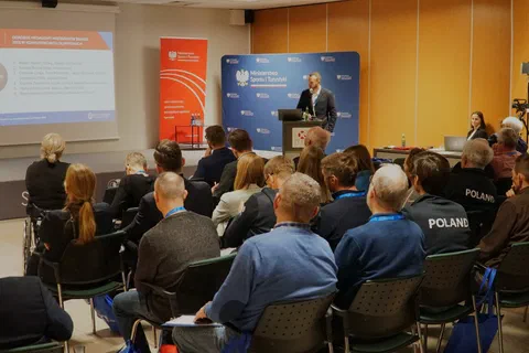 Wystąpienie przy mównicy przed trenerami zgromadzonymi w sali konferencyjnej.