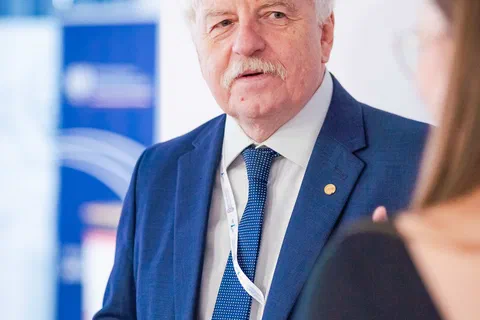 Mężczyzna w granatowym garniturze podczas wystąpienia przed uczestnikami konferencji.