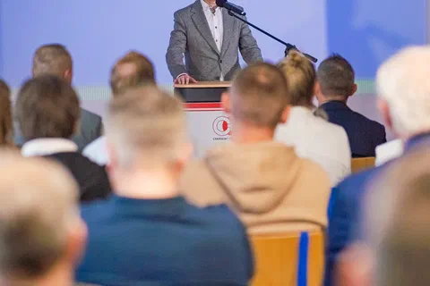 Wystąpienie przy mównicy na tle niebieskiej ścianki Ministerstwa Sportu i Turystyki.