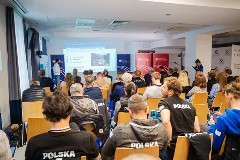 Sala konferencyjna wypełniona trenerami i uczestnikami słuchającymi prezentacji.