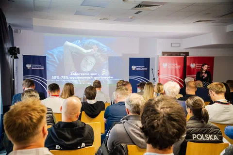 Prelegentka przy mównicy omawiająca slajd o zaburzeniach snu u wyczynowych sportowców.