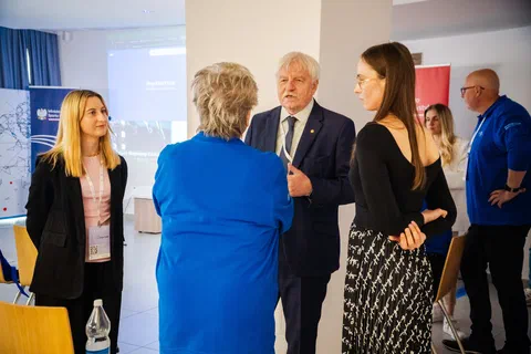 Rozmowa pięciorga uczestników konferencji w kuluarach sali wykładowej.