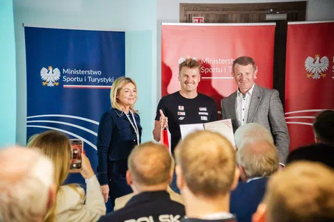 Wręczenie wyróżnienia trenerowi na tle banerów Ministerstwa Sportu i Turystyki.