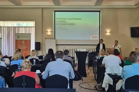 Dwaj prelegenci stojący przy ekranie z prezentacją o wybranych zagadnieniach z zakresu rachunkowości.